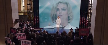 Movie still from “Long Shot” (2019), directed by Jonathan Levine – A woman standing at a podium in front of an image of a woman; Wide shot, Low angle