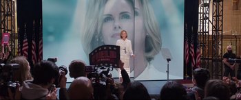 Movie still from “Long Shot” (2019), directed by Jonathan Levine – A woman standing in front of a microphone on a stage; Medium shot, Over the shoulder angle