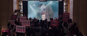 Movie still from “Long Shot” (2019), directed by Jonathan Levine – A crowd of people are gathered in front of a large screen; Wide shot, High angle