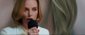 Movie still from “Long Shot” (2019), directed by Jonathan Levine – A woman is holding a microphone up to her mouth; Close Up shot, Over the shoulder angle