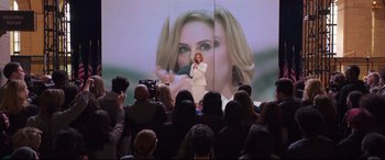 Movie still from “Long Shot” (2019), directed by Jonathan Levine – A crowd of people are gathered around to watch a woman speak; Wide shot, Over the shoulder angle