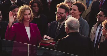 Movie still from “Long Shot” (2019), directed by Jonathan Levine – A group of people standing around each other holding a book; Medium shot, Over the shoulder angle