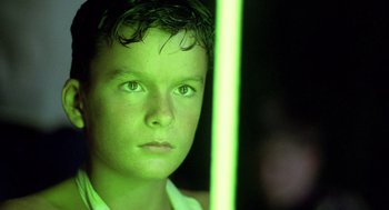 Movie still from “Lord of the Flies” (1990), directed by Harry Hook – A young boy is looking at the camera; Close Up shot, Low angle