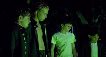 Movie still from “Lord of the Flies” (1990), directed by Harry Hook – A group of young men standing next to each other in the dark; Medium shot, Over the shoulder angle