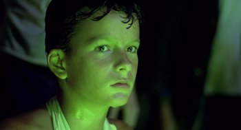 Movie still from “Lord of the Flies” (1990), directed by Harry Hook – A young boy is looking into the distance with green light; Close Up shot, Low angle