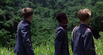 Movie still from “Lord of the Flies” (1990), directed by Harry Hook – Three young men are standing in front of a lush green forest; Medium shot, Over the shoulder angle