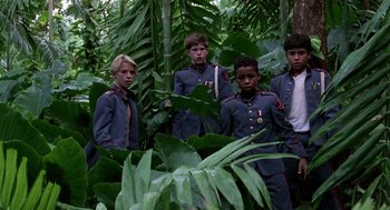 Movie still from “Lord of the Flies” (1990), directed by Harry Hook – A group of young men standing next to each other in a forest; Wide shot, High angle