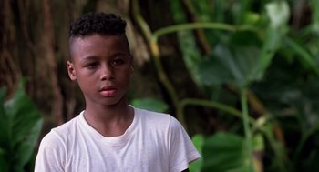 Movie still from “Lord of the Flies” (1990), directed by Harry Hook – A young boy is standing in front of some plants; Close Up shot, High angle