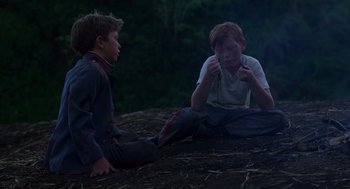 Movie still from “Lord of the Flies” (1990), directed by Harry Hook – Two young boys sitting on the ground in a field; Medium shot, High angle
