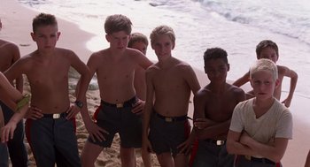 Movie still from “Lord of the Flies” (1990), directed by Harry Hook – A group of young men standing next to each other on the beach; Medium shot, Low angle