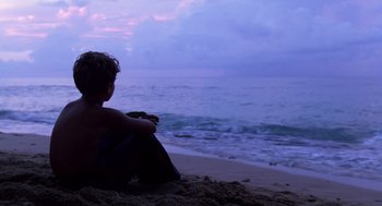 Movie still from “Lord of the Flies” (1990), directed by Harry Hook – A man sitting on the beach looking out at the ocean; Wide shot, Over the shoulder angle