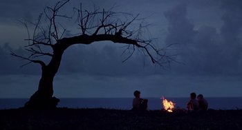 Movie still from “Lord of the Flies” (1990), directed by Harry Hook – A man sitting on the ground next to a fire; Extreme Wide shot, Low angle