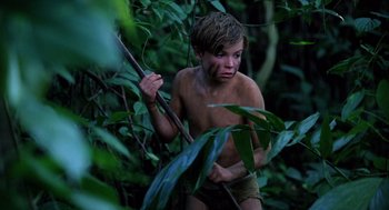 Movie still from “Lord of the Flies” (1990), directed by Harry Hook – A young boy in the woods holding a stick; Medium shot, High angle