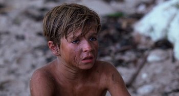Movie still from “Lord of the Flies” (1990), directed by Harry Hook – A young boy with wet hair sitting on the ground; Close Up shot, High angle