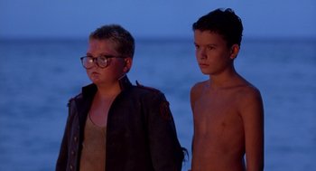 Movie still from “Lord of the Flies” (1990), directed by Harry Hook – Two young men standing next to each other on the beach; Medium shot, Low angle