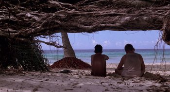 Movie still from “Lord of the Flies” (1990), directed by Harry Hook – Two people sitting under a tree on the beach; Wide shot, Low angle
