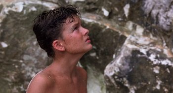 Movie still from “Lord of the Flies” (1990), directed by Harry Hook – A young man with wet hair is standing in a pool of water; Close Up shot, Low angle