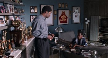Movie still from “Love & Basketball” (2000), directed by Gina Prince-Bythewood – Two men are sitting in a room with trophies on the wall; Wide shot, Over the shoulder angle