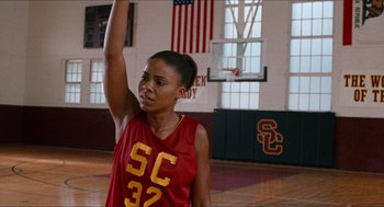 Movie still from “Love & Basketball” (2000), directed by Gina Prince-Bythewood – A woman in a red and yellow basketball uniform raises her arm in the air; Medium shot, Over the shoulder angle