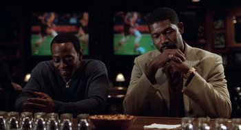 Movie still from “Love & Basketball” (2000), directed by Gina Prince-Bythewood – A couple of men sitting at a table in front of a tv; Medium shot, Over the shoulder angle