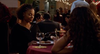 Movie still from “Love & Basketball” (2000), directed by Gina Prince-Bythewood – A woman sitting at a table with a plate of food; Medium shot, Over the shoulder angle