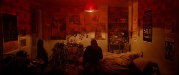 Movie still from “Love” (2015), directed by Gaspar Noé – A person sitting on a bed under a red light; Wide shot, Overhead angle