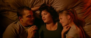 Movie still from “Love” (2015), directed by Gaspar Noé – A man and two women laying in a bed together; Medium shot, Overhead angle