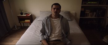 Movie still from “Love” (2015), directed by Gaspar Noé – A man sitting on top of a bed in front of a window; Medium shot, High angle