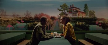 Movie still from “Love” (2015), directed by Gaspar Noé – A man and a woman sitting at a table with a cup of coffee; Medium shot, High angle