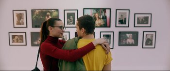 Movie still from “Love” (2015), directed by Gaspar Noé – A woman and a young man standing next to each other in front of pictures; Medium shot, Over the shoulder angle