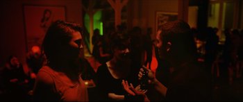 Movie still from “Love” (2015), directed by Gaspar Noé – A group of people standing in a dark room; Medium shot, Over the shoulder angle