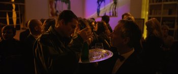 Movie still from “Love” (2015), directed by Gaspar Noé – A man sitting at a table with a tray of wine; Medium shot, Over the shoulder angle