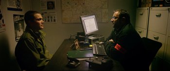Movie still from “Love” (2015), directed by Gaspar Noé – A man sitting in front of a computer on top of a desk; Medium shot, Over the shoulder angle