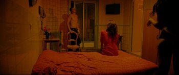 Movie still from “Love” (2015), directed by Gaspar Noé – A man and a woman sitting on a bed in front of a door; Wide shot, High angle