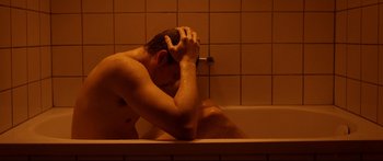 Movie still from “Love” (2015), directed by Gaspar Noé – A man sitting in a bath tub with his hands on his head; Medium shot, High angle