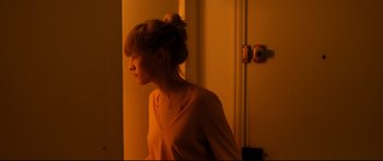 Movie still from “Love” (2015), directed by Gaspar Noé – A woman standing next to a door in a room; Medium shot, High angle