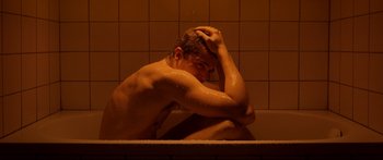 Movie still from “Love” (2015), directed by Gaspar Noé – A man sitting in a bath tub with his hands on his head; Medium shot, High angle