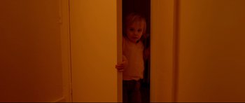 Movie still from “Love” (2015), directed by Gaspar Noé – A little girl standing in a doorway looking at the camera; Medium shot, High angle