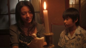 Movie still from “Love Exposure” (2008), directed by Sion Sono – A woman and a boy are looking at a candle; Close Up shot, Over the shoulder angle