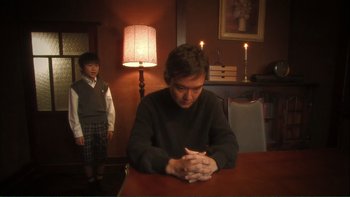 Movie still from “Love Exposure” (2008), directed by Sion Sono – A man sitting at a table in front of a boy; Medium shot, Low angle