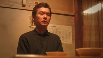 Movie still from “Love Exposure” (2008), directed by Sion Sono – A man sitting at a table with a bowl in front of him; Close Up shot, Low angle
