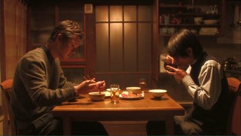 Movie still from “Love Exposure” (2008), directed by Sion Sono – A man and a woman sitting at a dinner table looking at cell phones; Medium shot, Low angle