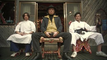 Movie still from “Love Exposure” (2008), directed by Sion Sono – A man sitting on top of a wooden bench; Medium shot, Low angle