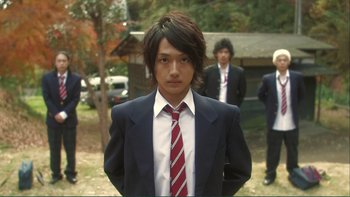 Movie still from “Love Exposure” (2008), directed by Sion Sono – A man in a suit and tie standing in front of other men; Close Up shot, Low angle