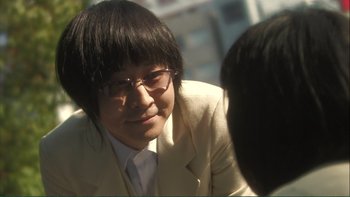 Movie still from “Love Exposure” (2008), directed by Sion Sono – A young man wearing a suit and glasses; Close Up shot, Over the shoulder angle