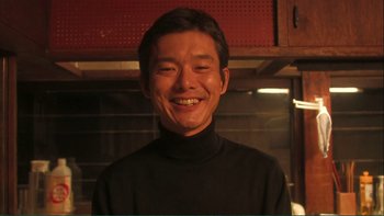 Movie still from “Love Exposure” (2008), directed by Sion Sono – A young man smiling for the camera in a kitchen; Close Up shot, Low angle
