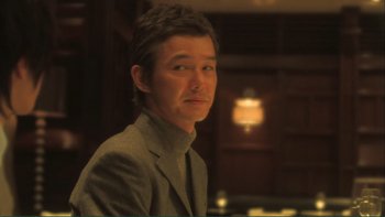 Movie still from “Love Exposure” (2008), directed by Sion Sono – A man wearing a suit and tie in front of a table; Close Up shot, Low angle