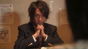 Movie still from “Love Exposure” (2008), directed by Sion Sono – A man in a suit sitting at a dinner table; Close Up shot, Over the shoulder angle