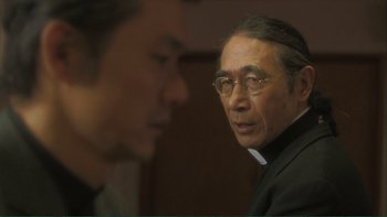 Movie still from “Love Exposure” (2008), directed by Sion Sono – A man wearing glasses and a priest's outfit; Close Up shot, Over the shoulder angle