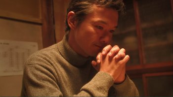 Movie still from “Love Exposure” (2008), directed by Sion Sono – A man in a sweater is holding his hands in prayer; Close Up shot, Low angle